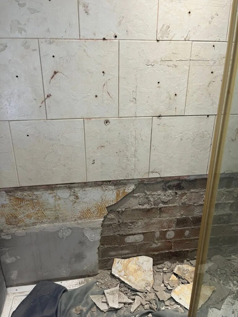 Water-damaged shower wall exposed before damp repair in Newcastle