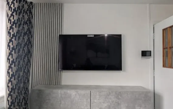 Wall-mounted TV with floating grey media unit, decorative slatted panel and neatly arranged cables in Newcastle